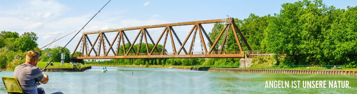 Ein Angler sitzt am Kanal. Im Hintergrund sieht man eine Brücke.