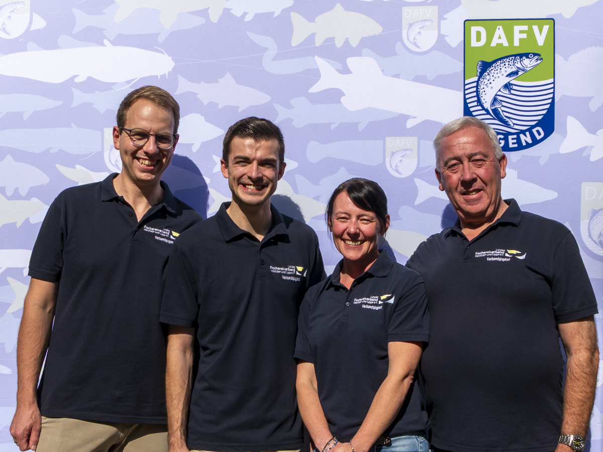 Vier Personen stehen vor einer Logowand.